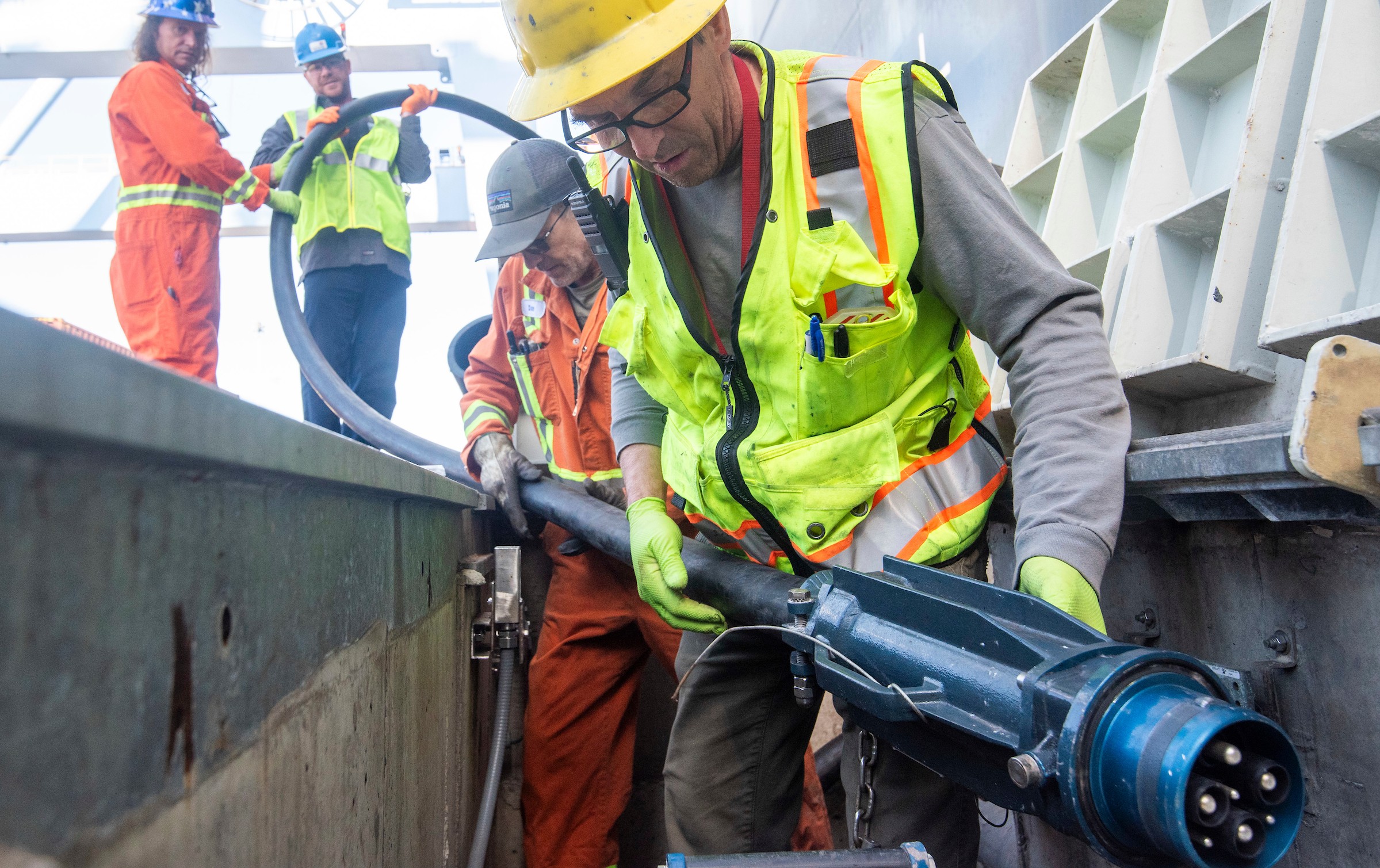 Four men hold a large electrical cord while wearing safety gear.